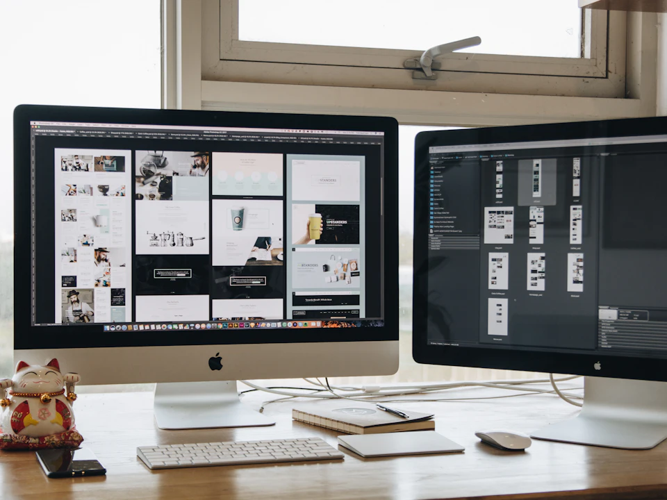 Two monitors on a desk showing web page designs