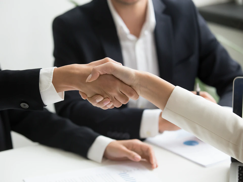 Two people shaking hands over a laptop after a deal